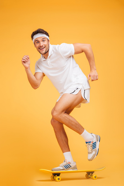 Full length portrait of a happy young sports man skateboarding - Фото, изображение