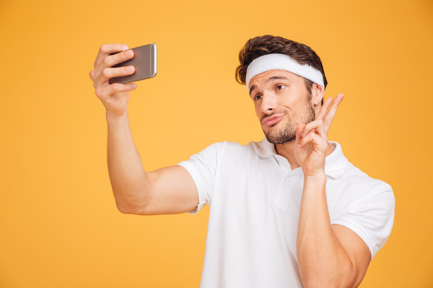 Smiling young sports man taking selfie and showing v sign - Fotó, kép