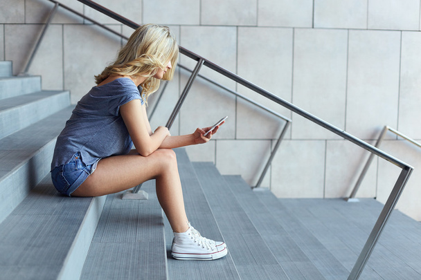 Chica escribiendo mensaje en el teléfono móvil y sentado en las escaleras
 - Foto, Imagen