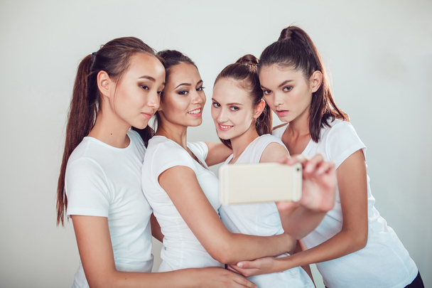 Positive friends portrait of four happy girls making selfie, sure funny faces, grimaces, joy, emotions, casual style, pastel colors, white wall. crazy funny woman. White background. - Фото, изображение
