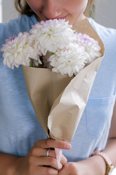 Nahaufnahme eines unkenntlichen Mädchens, das einen Strauß weißer Blumen in Bastelpapier riecht - Foto, Bild