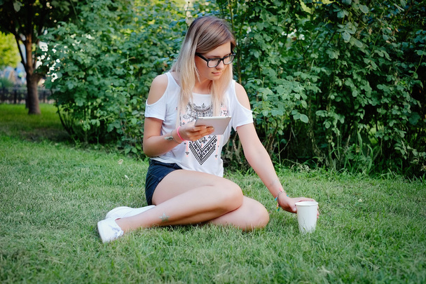 das Mädchen, das mit Tablette in der Hand auf dem Gras sitzt - Foto, Bild