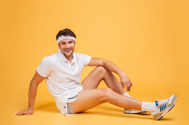 Full length of cheerful attractive young sportsman sitting and smiling - Foto, immagini