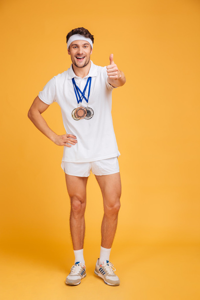 Happy spotrsman with three medals standing and showing thumbs up - Fotoğraf, Görsel