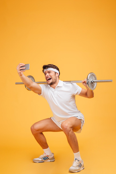 Sportsman training with barbell and talking selfie using cell phone - Foto, immagini