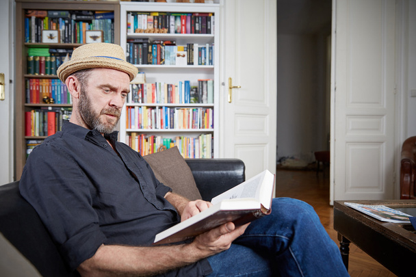 Man with beard reading a book in his living room - Photo, Image