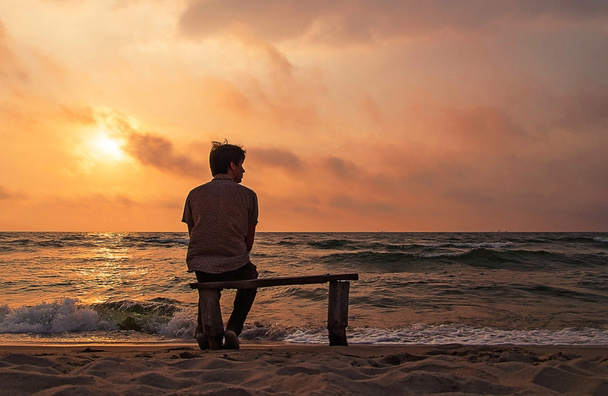Un homme seul assis sur un banc sur la côte profitant du coucher de soleil
 - Photo, image
