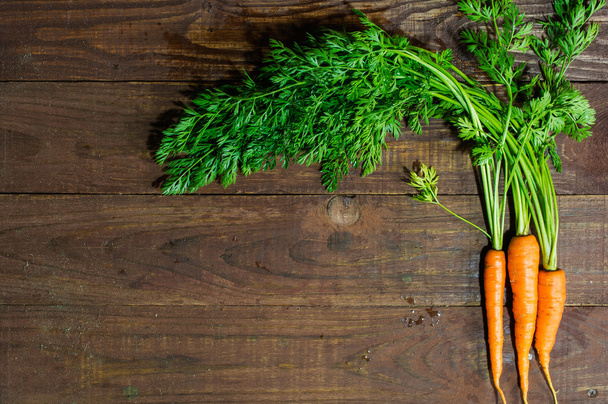 bunch of fresh harvested carrots with green leaves on wooden table background - Foto, Imagen