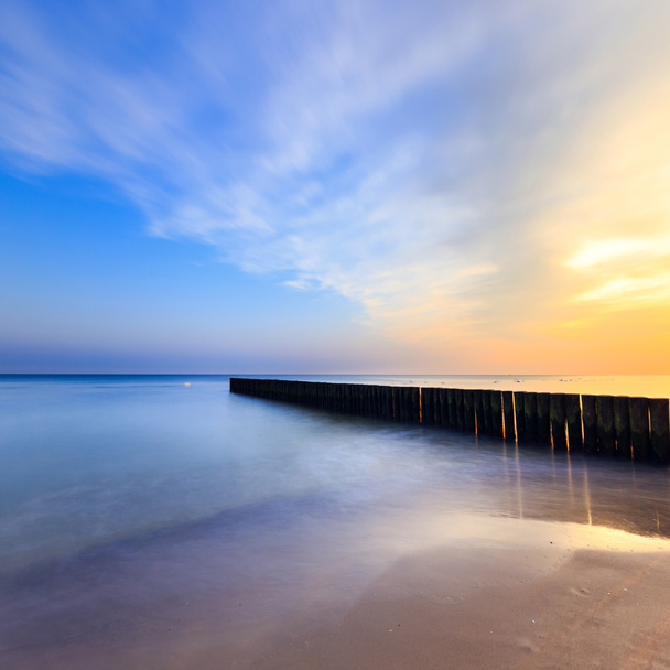 pôr do sol na praia com um quebra-mar de madeira, longa exposição
 - Foto, Imagem