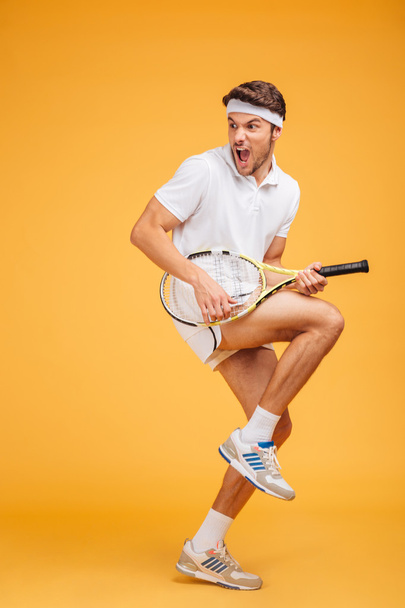 Comical young man tennis player with racket shouting and joking - Fotó, kép