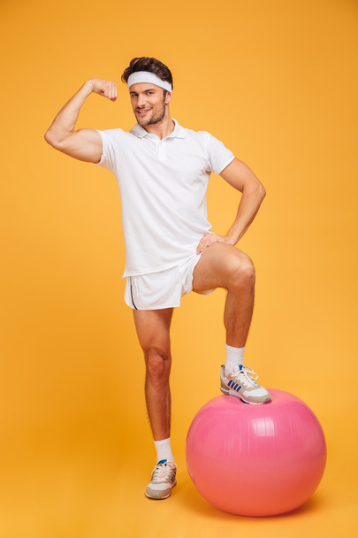 Young handsome sportsman with fitness ball showing biceps - Foto, afbeelding