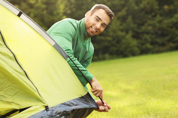 Nuori mies pystyttämässä telttaa
 - Valokuva, kuva