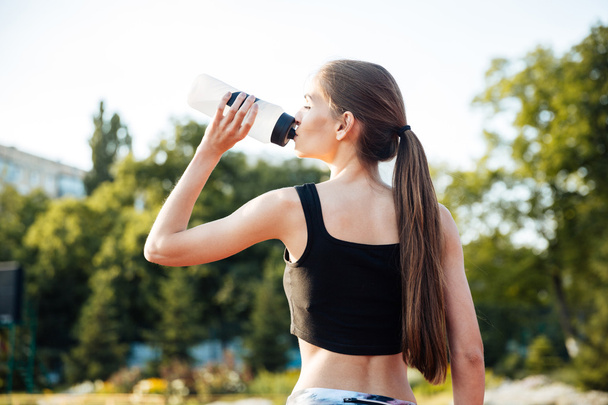 Female athlete drinking from water bottle after workout at stadium - Fotó, kép