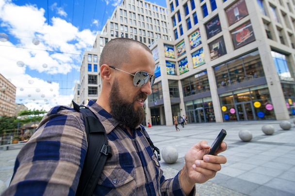 νέοι γενειοφόρος άνδρας βλέπει το smartphone για το φόντο της πόλης,  - Φωτογραφία, εικόνα