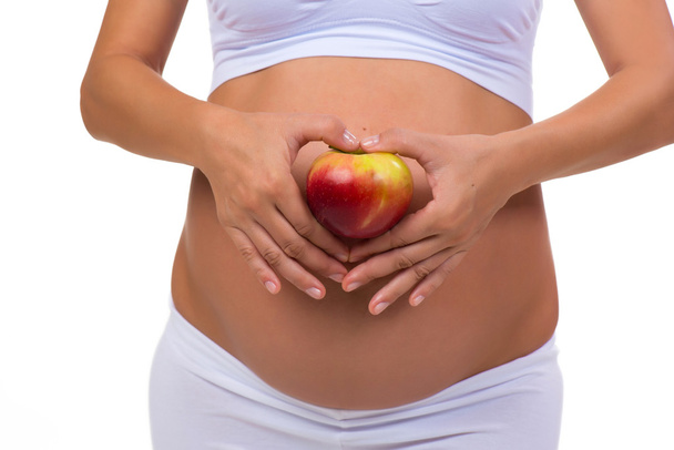 Close-up of a pregnant belly and apple. Hands folded heart. On a white background - Fotoğraf, Görsel