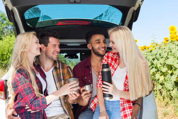 Friends drinking tea holding coffee cups thermos sitting in car trunk outdoor countryside - Foto, Imagem