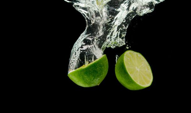 Two halves of lime into the water drop. - Foto, afbeelding
