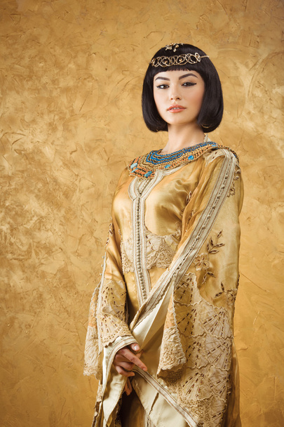 Beautiful woman like Egyptian Queen Cleopatra on golden background - Foto, imagen