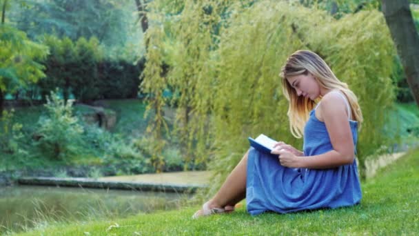 Молодая привлекательная женщина читает книгу в парке, сидя на траве
 - Кадры, видео