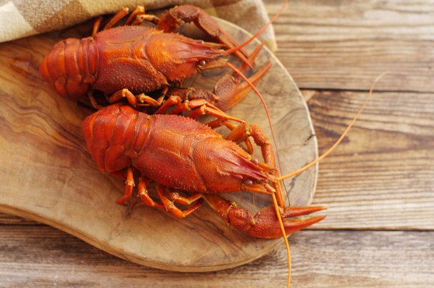 Boiled crawfishes on a wooden board on a wooden background - Foto, afbeelding