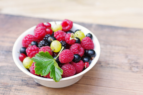 Fresh juicy berries, raspberries, currants, blackberries, a gooseberry in an white plate  - Fotografie, Obrázek