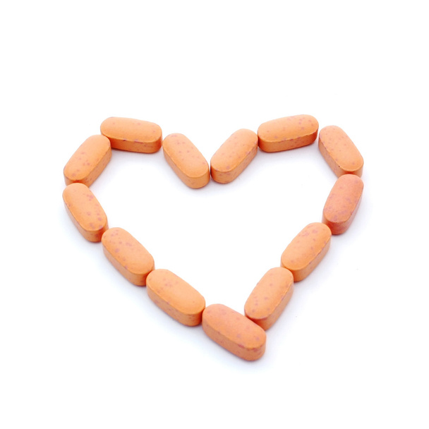Orange pills in heart shape isolated on white background with co - Foto, immagini
