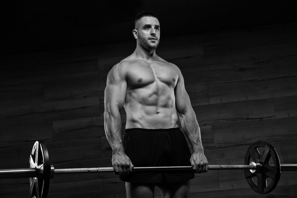 Όμορφος άντρας με μεγάλους μυς, ποζάρει στην κάμερα του γυμναστηρίου. - Φωτογραφία, εικόνα