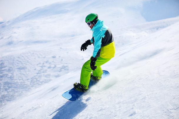 snowboarder συρόμενη κάτω από μια κλίση σε μια ηλιόλουστη ημέρα - Φωτογραφία, εικόνα