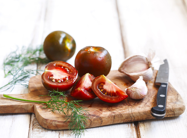 Whole, cut tomatoes and garlic in cutting board - Фото, зображення