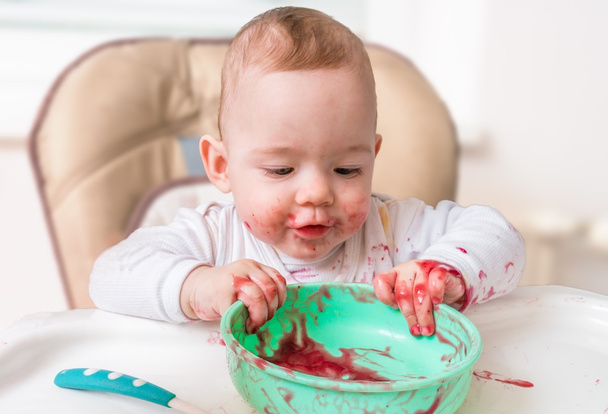 Messy and dirty baby is eating from bowl. - Photo, Image
