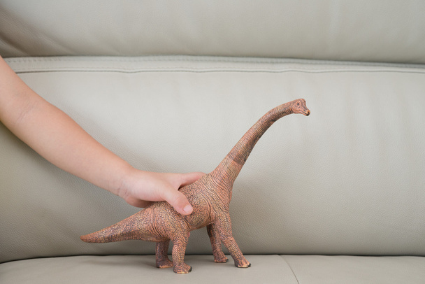 çocuklar el evde kanepede bir brachiosaurus oyuncak yakalamak - Fotoğraf, Görsel