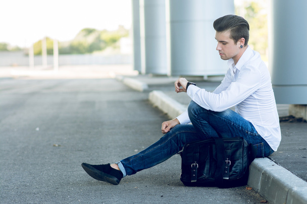 csinos, fiatal férfi használ smartphone út mellett ülve - Fotó, kép