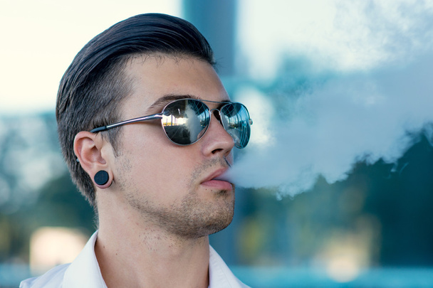 Young man smoking electronic cigarette outdoors - 写真・画像
