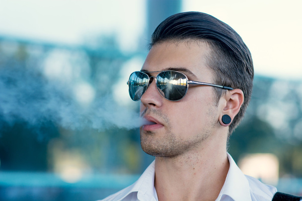 Young man smoking electronic cigarette outdoors - 写真・画像