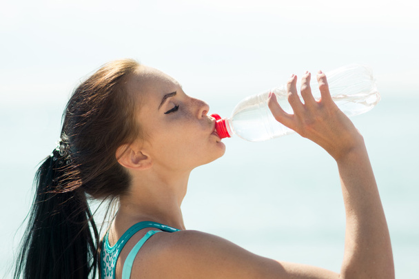 Fitness woman drinking water after running at beach - Zdjęcie, obraz