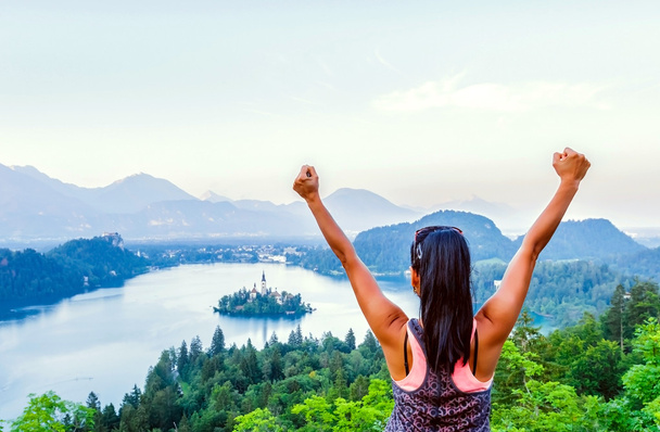 woman standing, raising hands and looking at beautiful view of lake Bled - Photo, Image