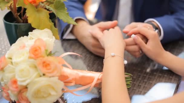 Hands of bride and groom with wedding rings on wooden table with bouquet of roses - Footage, Video