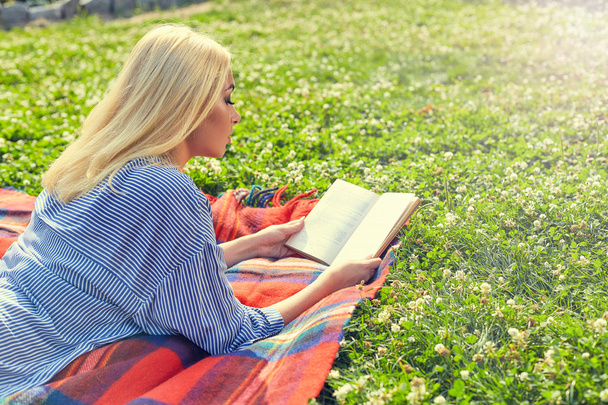 Perfil da menina loira ler livro na grama verde
 - Foto, Imagem