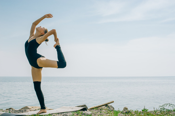 young woman is engaged in meditation, stretching, yoga on the beach background - 写真・画像