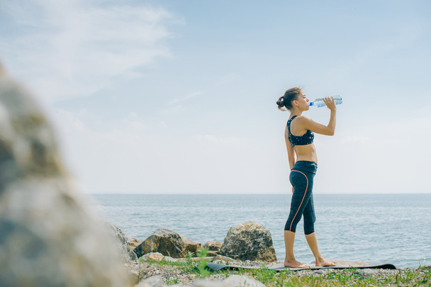 athletic girl drinks water from a bottle on the shore after a workout - Valokuva, kuva