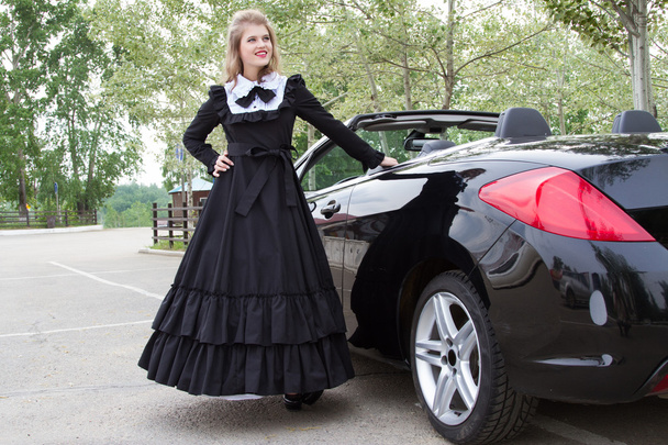 Mädchen in altem langen Kleid steht neben dem modernen Auto - Foto, Bild