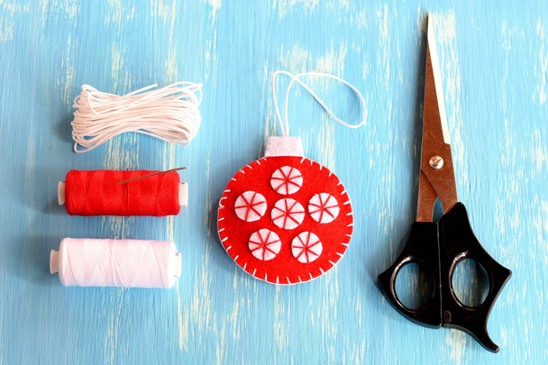 Felt Christmas tree ball, scissors, white and red threads, cord on blue wooden background. Hand made Christmas tree ornament diy. Felt crafts tutorial. Step. Top view. Handwork crafts for kids at home photo. Children craft making - Photo, Image