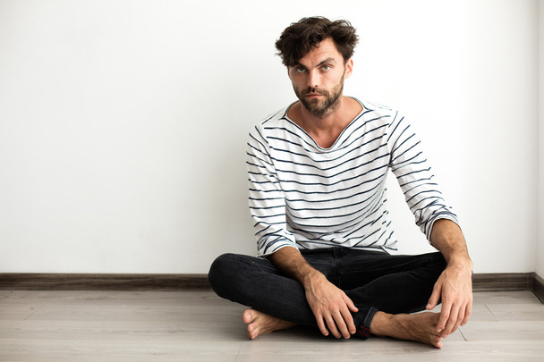 Handsome man in stripes sitting down on the floor - Фото, изображение