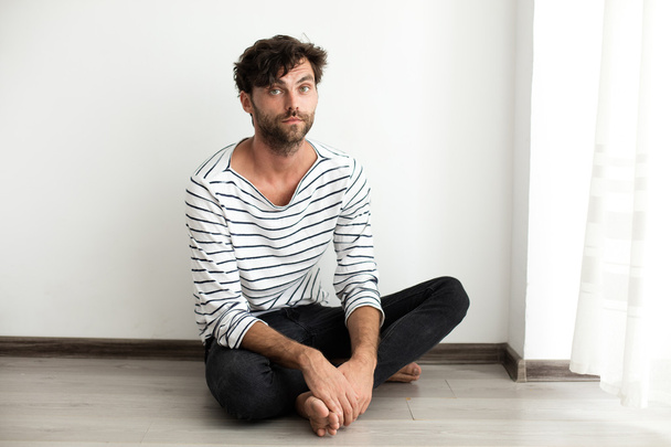Handsome man in stripes sitting down on the floor - Фото, зображення