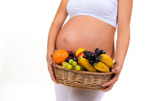 Close-up of a pregnant belly and a basket of exotic fruits. Healthy pregnancy, vitamins. - Фото, изображение