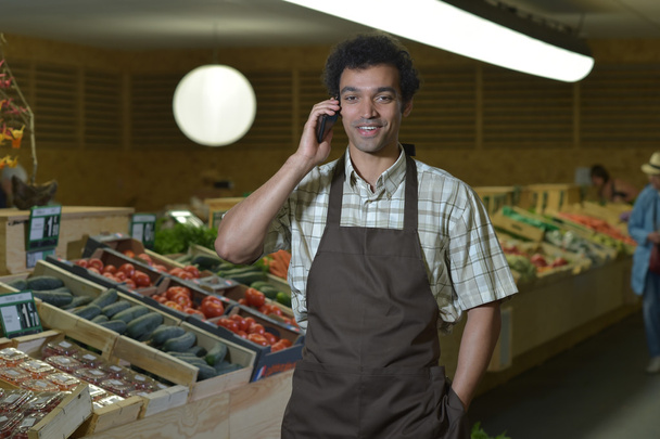 Grocery clerk phoning in produce aisle of supermarket store - 写真・画像