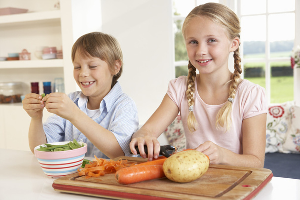 Happy children peeling vegetables in kitchen - 写真・画像
