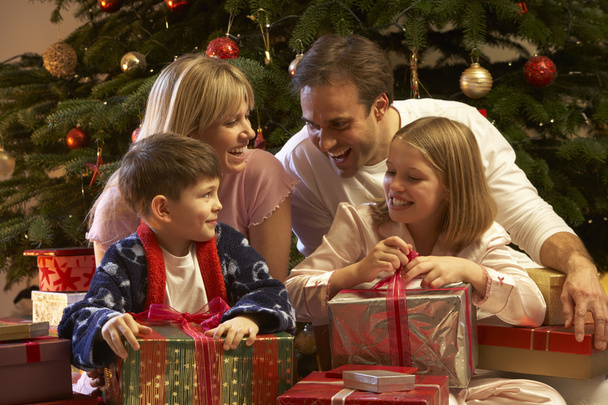 Family Opening Christmas Present In Front Of Tree - 写真・画像