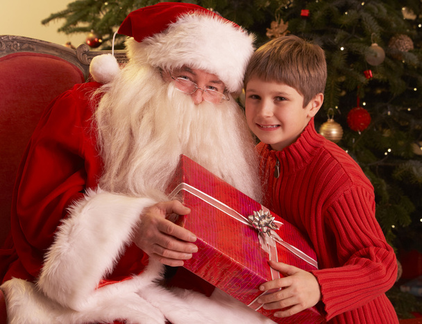 Santa Claus Giving Gift To Boy In Front Of Christmas Tree - Foto, afbeelding