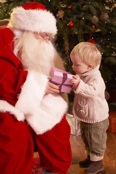 Santa Claus Giving Gift To Boy In Front Of Christmas Tree - Foto, imagen